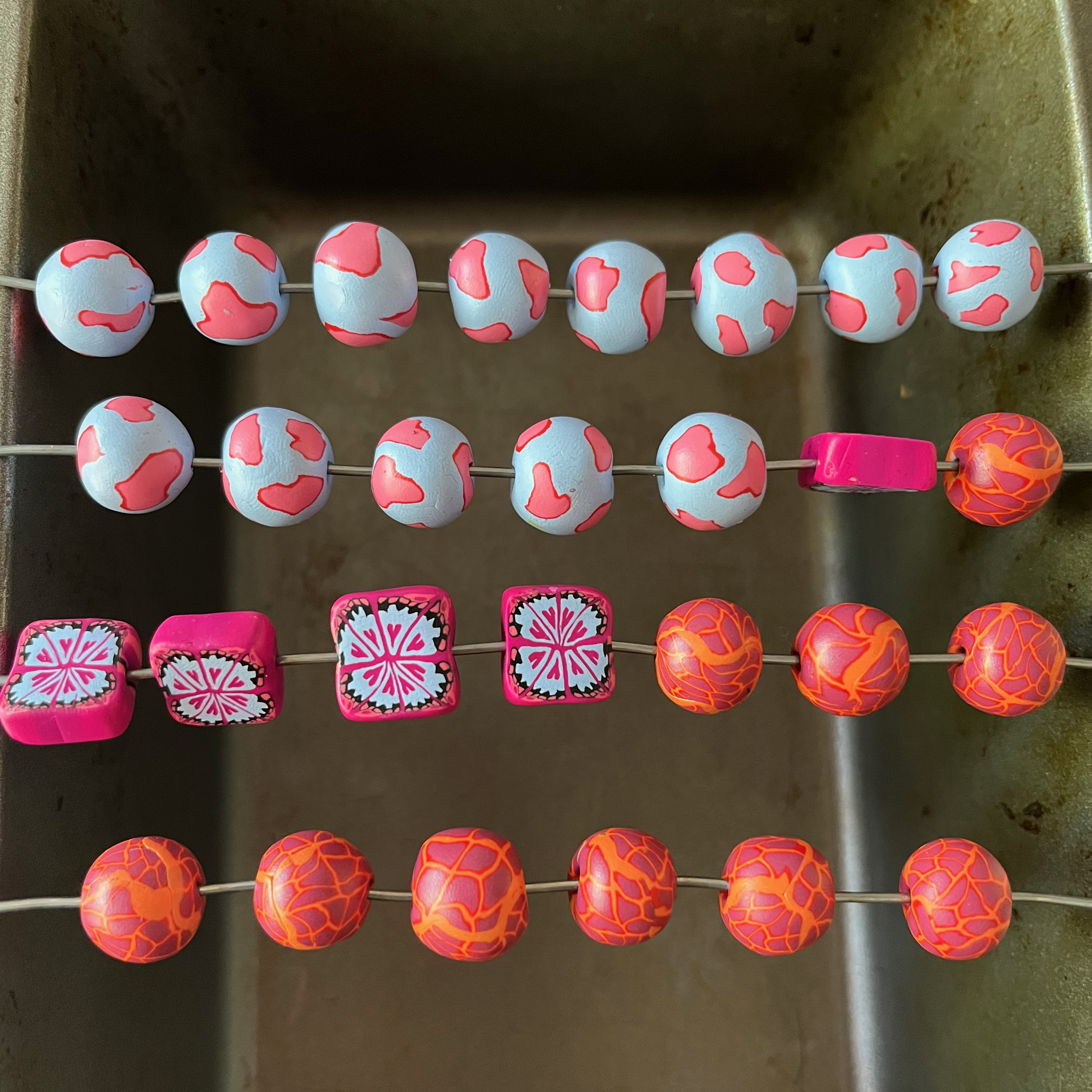 An image of a baking pan turned into a makeshift rack with some marbled polymer clay beads waiting to be baked.